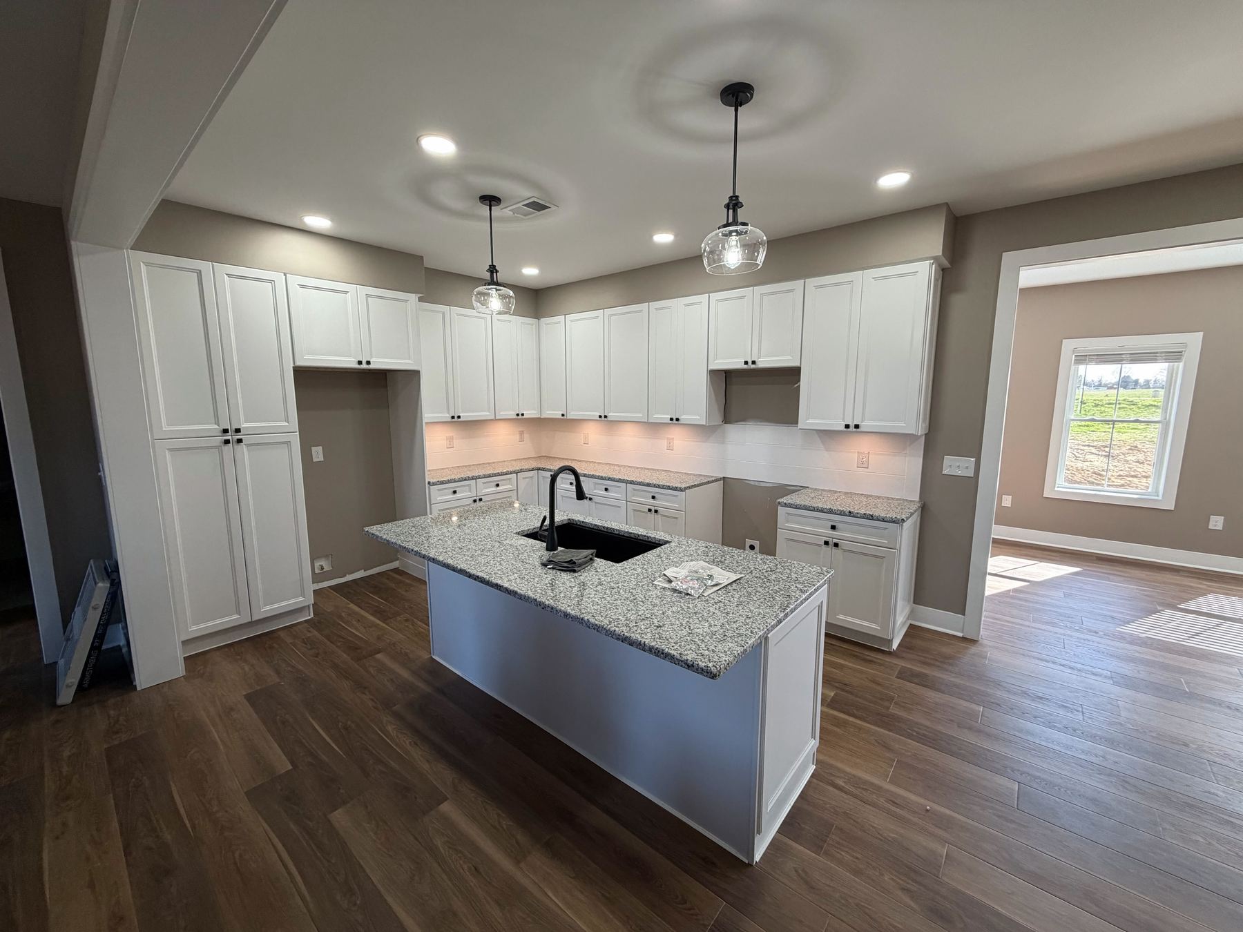 New home kitchen with white shaker cabinets, granite island, and wide-plank flooring